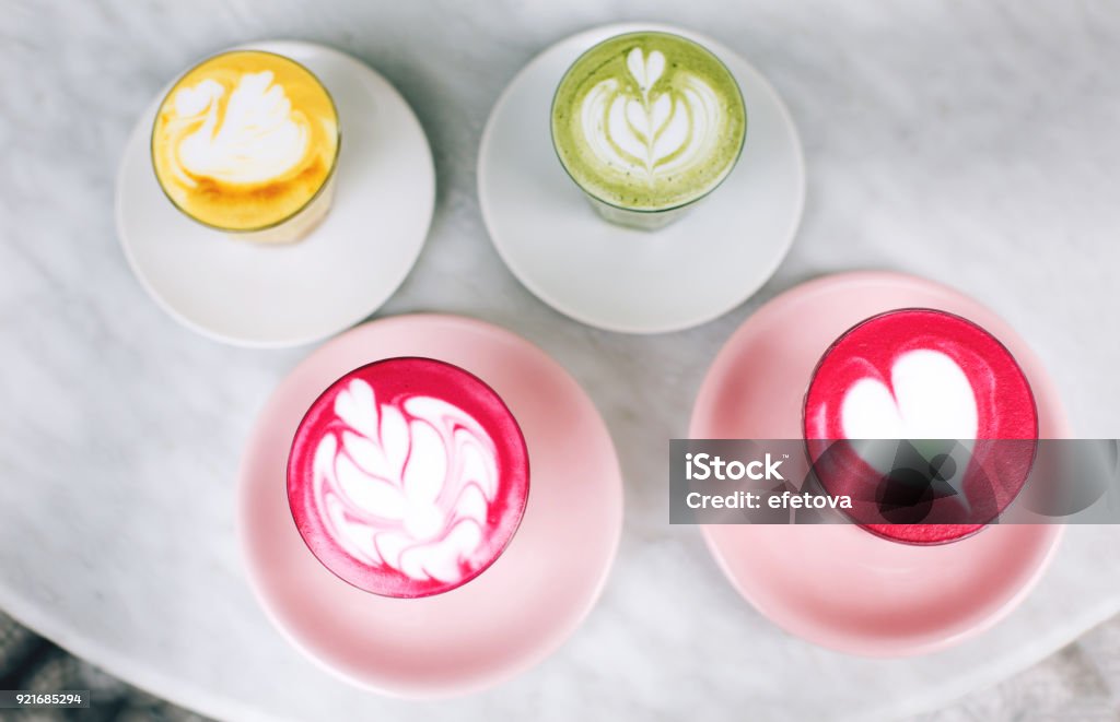 Two beetroot lattes Trendy multicolored lattes. Beetroot, avocado and turmeric tastes with latte art and flower petals on foam. Latte Stock Photo