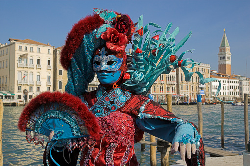 Venice, Italy - March 01, 2022: Woman dressed in traditional costume stand in front of the Bridge of Sighs, part of the Venice Mask Carnival, Veneto, Italy