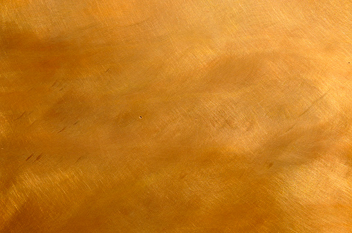 Abstract brushed brown-golden copper or bronze surface, with visible brush strokes. The sheet metal has an appealing cloudy, mottled texture. Horizontal orientation. The image has been shot outdoors during natural day light, full frame and close up. Ideal for backgrounds. The dimensions of the photo are 3300 x 2192 px
