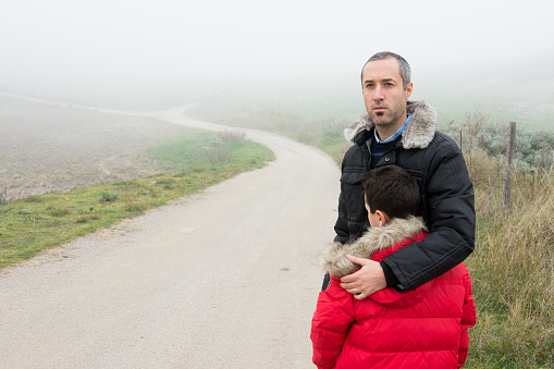 Concept of family escaping.  Father and son in a mountain road with fog. Scene with actors