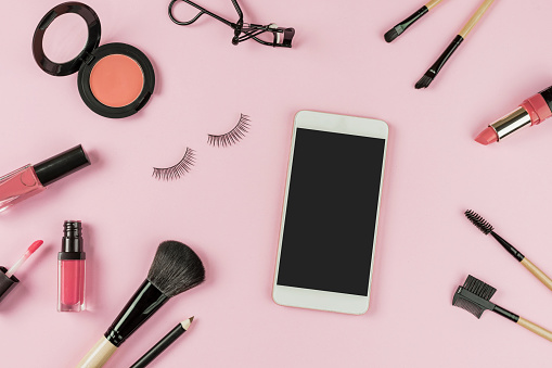 Set of make up brushes and cosmetics on pink background with smart phone and copy space, Top view