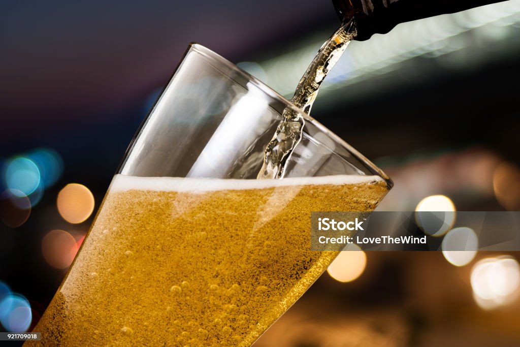 Motion of beer pouring from bottle into glass on bokeh light night background Beer - Alcohol Stock Photo