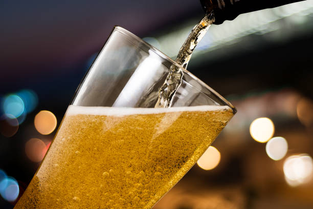 Motion of beer pouring from bottle into glass on bokeh light night background Motion of beer pouring from bottle into glass on bokeh light night background beaker pour stock pictures, royalty-free photos & images
