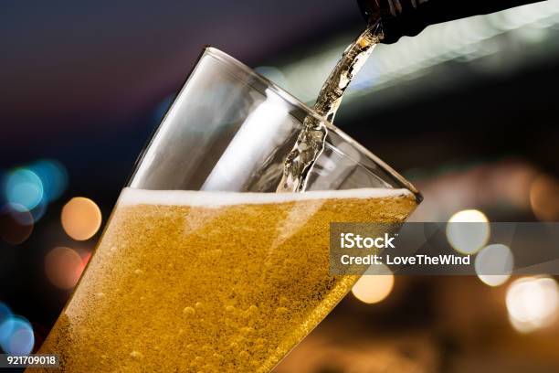 Motion Of Beer Pouring From Bottle Into Glass On Bokeh Light Night Background Stock Photo - Download Image Now