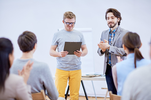 Business coach clapping his hands while looking at audience after report of young speaker at conference