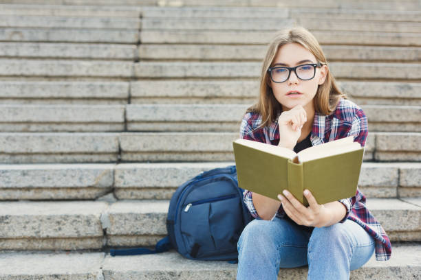 istock Young woman reading book on university stairs 921732954