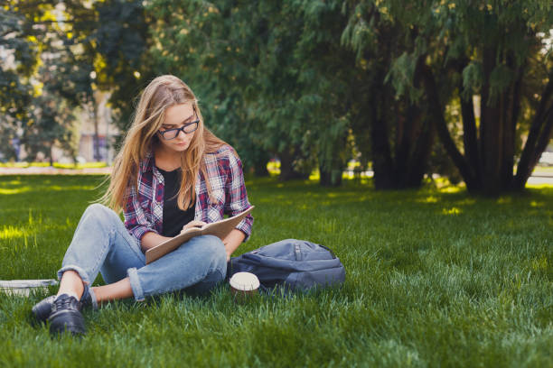 istock Young woman sitting with notebook on grass 921733502