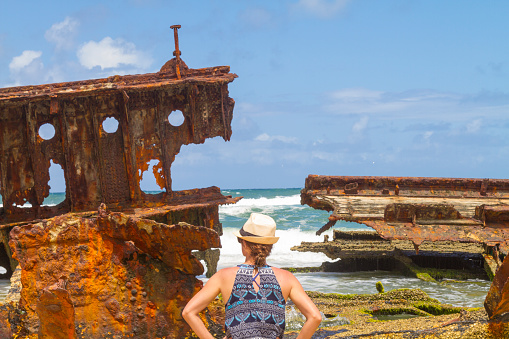 Young female traveler tourist taking a break in her vacations in front of Maheno shipwreck on Fraser Island, Queensland, Australia