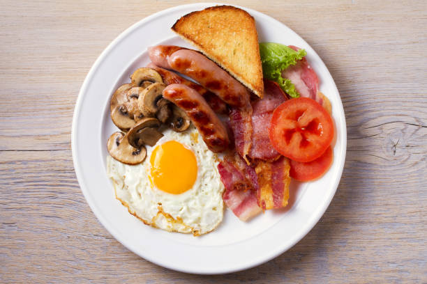 full english or irish breakfast: sausages, bacon, egg, mushrooms, tomatoes and toasts. nutritious morning meal - english tomato imagens e fotografias de stock