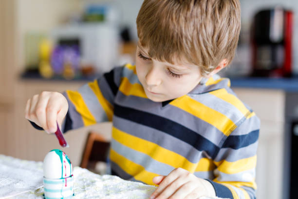 istock Little blond kid boy coloring eggs for Easter holiday in domestic kitchen, indoors. 921765866