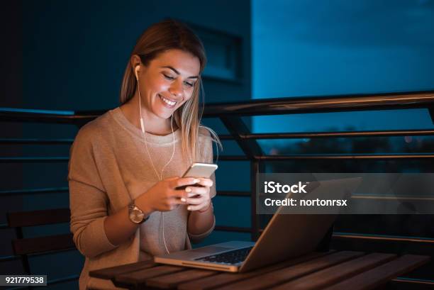 Young Beautiful Woman Using Phone And Listening Music At Evening In Her Home High Iso Image Stock Photo - Download Image Now