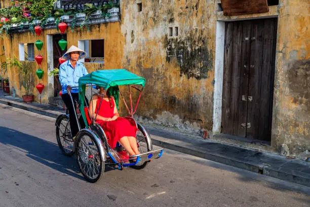 Vietnamese cycle rickshaw with caucasian young female tourist in old town in Hoi An city, Vietnam, old town in Hoi An city, Vietnam. Hoi An is situated on the east coast of Vietnam. Its old town is a UNESCO World Heritage Site because of its historical buildings.