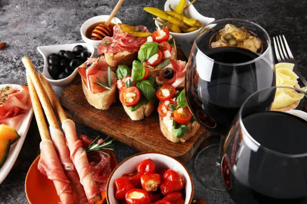 Italian antipasti wine snacks set. Cheese variety, Mediterranean olives, pickles, Prosciutto di Parma, tomatoes, artichokes and wine in glasses