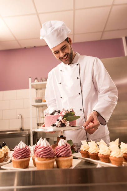 istock smiling confectioner standing at counter with cake and cupcakes in restaurant kitchen 921787924