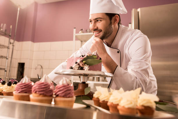 istock smiling confectioner standing at counter with cake and cupcakes in restaurant kitchen 921788454