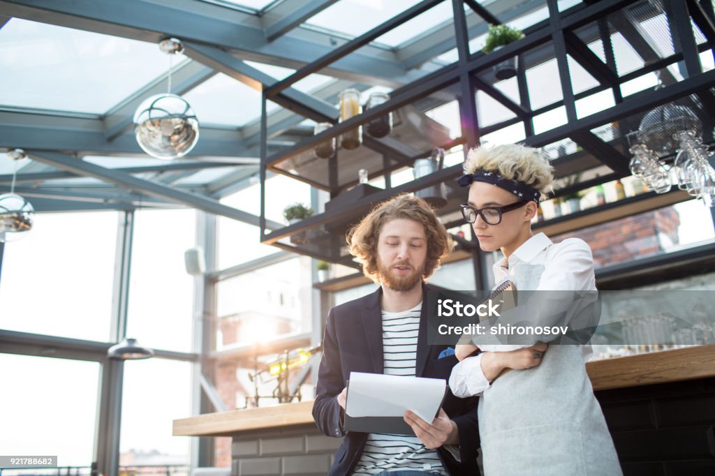 Showing contract to waitress Head manager of new modern restaurant showing working contract to young waitress and explaining her its terms Restaurant Stock Photo