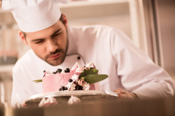istock selective focus of confectioner looking at cake in hands in restaurant kitchen 921789058