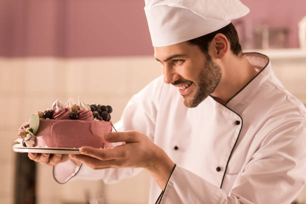 istock side view of smiling confectioner looking at cake in hands in restaurant kitchen 921789692