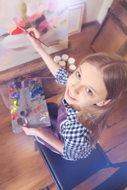 istock Chestnut haired girl smiling while painting 921802684
