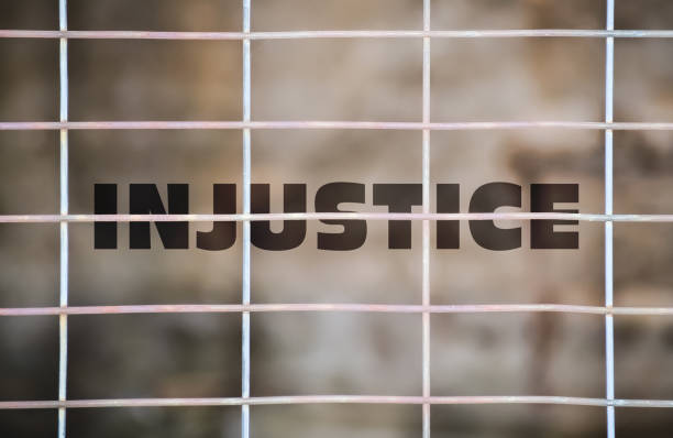 Word Injustice written under a wire fence and blurry background