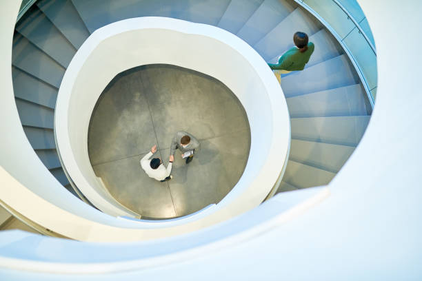 Business Deal Background Wide angle view at two business people shaking hands standing at bottom of winding staircase in modern office building, copy space co dependent relationship stock pictures, royalty-free photos & images