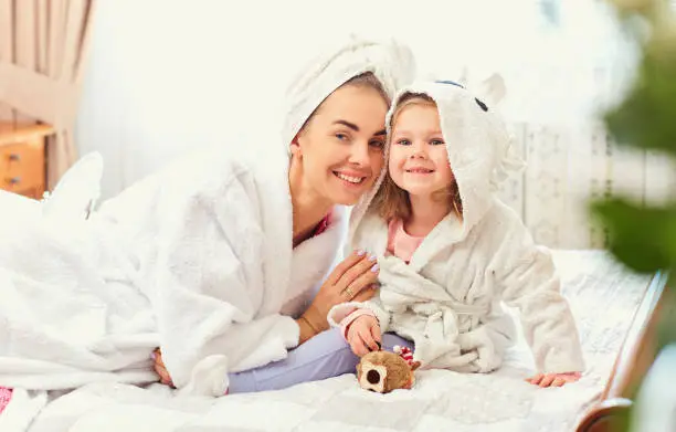 Photo of Mother and daughter in bathrobes and towels on the bed in the ro