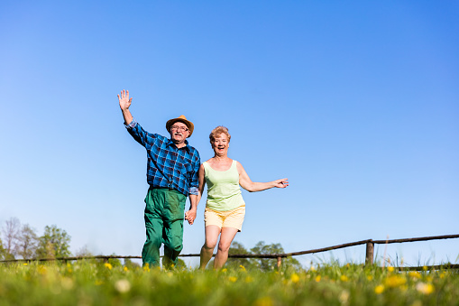 Senior couple holding hands and running on a green field in the summer. Mature love and relationship.