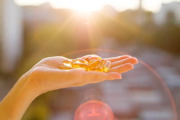 ręka kobiety trzymającej olej z ryb kapsułki omega-3, miejskie tło zachodu słońca. zdrowe odżywianie, medycyna, opieka zdrowotna, suplementy diety i pojęcie ludzi - nutritional supplement pill eating food zdjęcia i obrazy z banku zdjęć