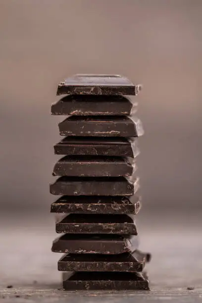 Chopped dark chocolate bars aligned as a tower on brown wooden background