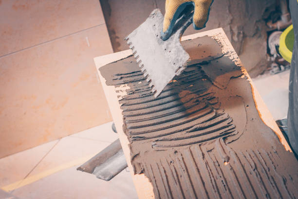 istock The working tiler applies glue on the tile with a notched trowel before gluing, the technology of tiling and finishing 921865532
