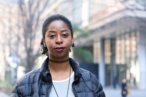 A young black woman in casual clothes looking at the camera confidently.