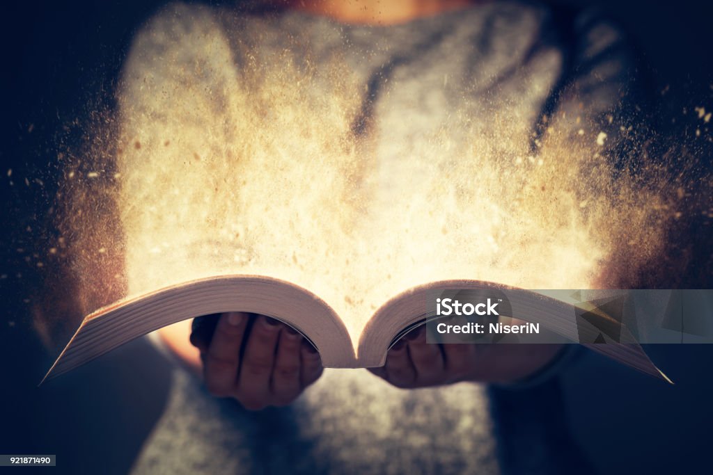 Woman holding an open book bursting with light. Woman holding an open book with two hands. Light coming out of the book as a concept of learning, education, knowledge and religion Storytelling Stock Photo