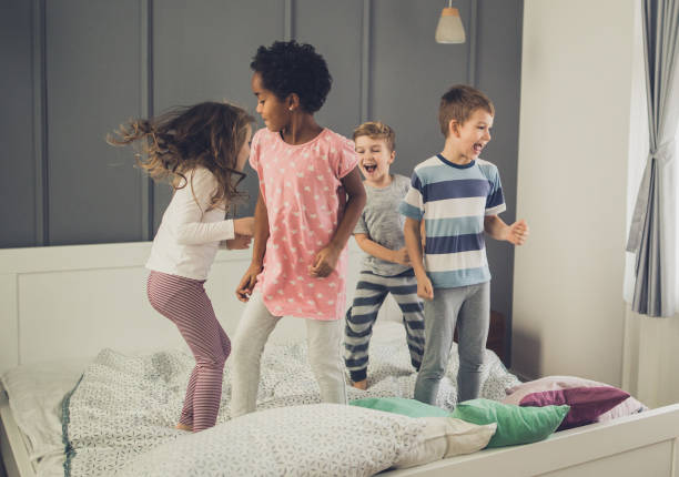 istock Small friends having fun in a bedroom while jumping on a bed. 921875800