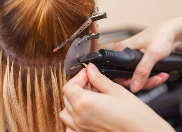 the hairdresser does hair extensions to a young girl, a blonde in a beauty salon. - strand imagens e fotografias de stock