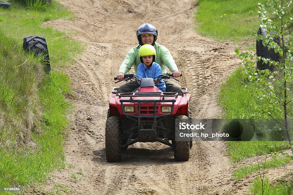 Father & son in helmets riding a quad bike on a track Dad with son riding a quad bike Quadbike Stock Photo