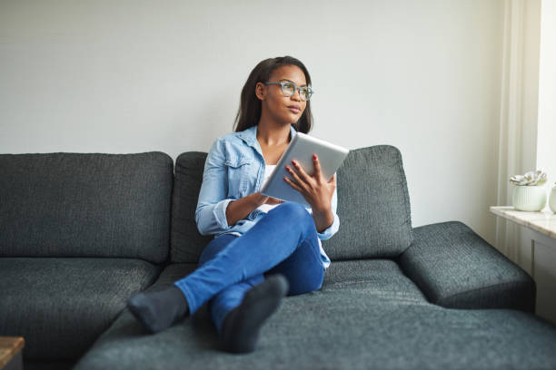 istock Young African woman relaxing on her sofa browsing the internet 921889602
