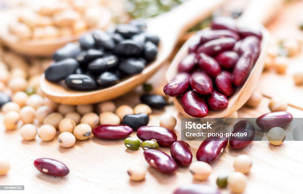 Many types of beans are separated in a spoon on a wood table such as mung bean, soybean, black bean, red bean. selective focus. Bean Stock Photo