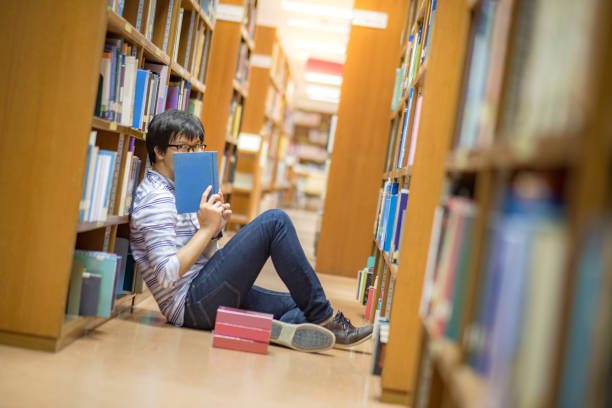 istock Young Asian man university student reading book in library 921892840
