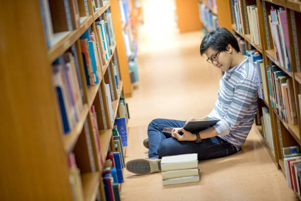 istock Young Asian man university student reading book in library 921892896
