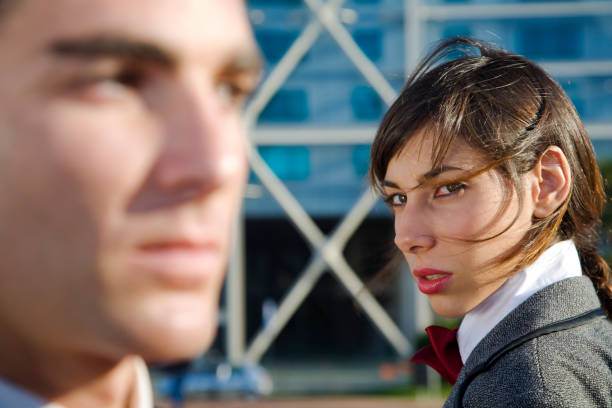 Woman looking at a man with distrust Businessman and bussinesswoman in distrust behaviour. She is in focus and he isn't. business battle stock pictures, royalty-free photos & images