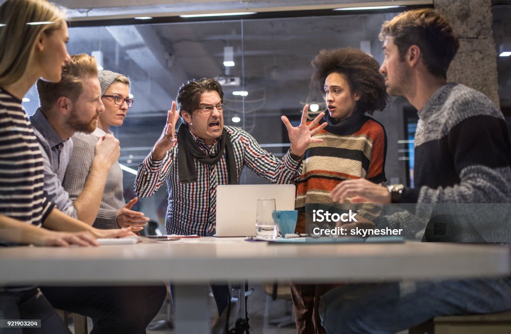 Furious boss shouting at his team on a meeting in the office. Angry manager shouting at his coworkers during a meeting in the office. Rudeness Stock Photo