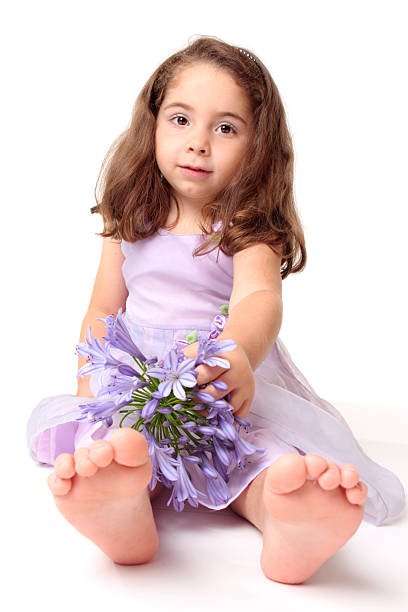 Close-up side view of a young girl smelling lilac blossoms on a lilac bush in full bloom. The girl has curly blonde hair and is using her hand to get the flowers closer to her face.