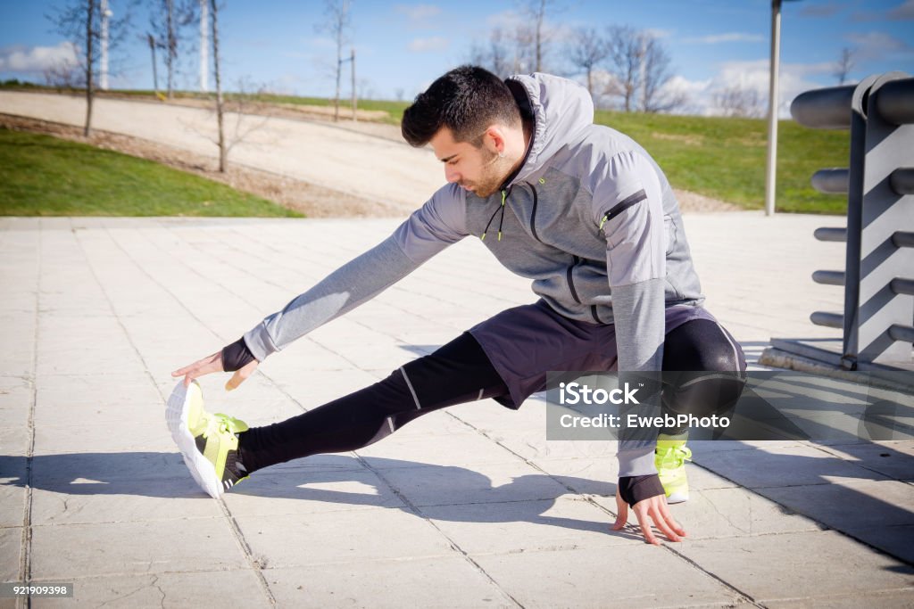 Young athletic man is preparing before running in a city park in winter. One young caucasian athletic man is preparing before running in a city park in winter. Active Lifestyle Stock Photo
