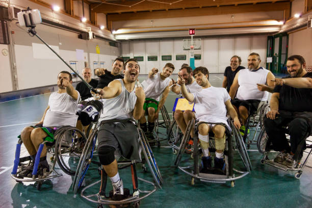 group of smiling disabled basketball players on a wheelchair take a selfie in a basketball court