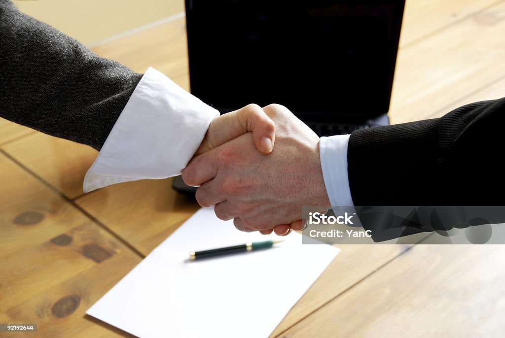 Business people shaking hands in agreement man and woman shaking hands in front of laptop Agreement Stock Photo