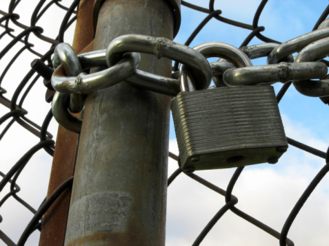 Lock and chain on an iron gate, and sky seen through the chain link fence.