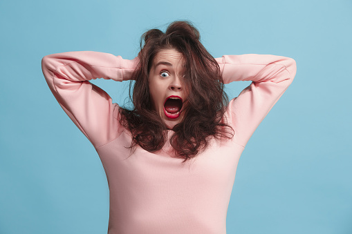 I lost my mind. Stress. The screaming woman with horror expression. Beautiful female half-length portrait isolated on blue studio backgroud. The crazy woman. The human emotions, facial expression concept.