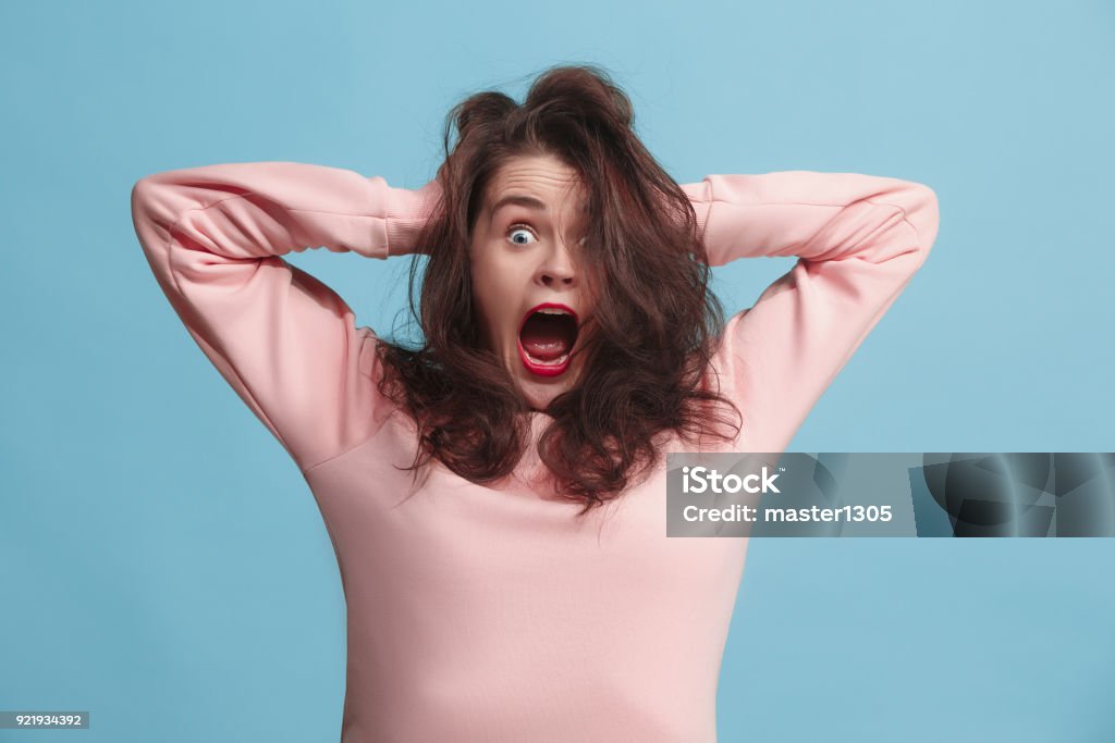 The squint eyed woman with weird expression isolated on blue I lost my mind. Stress. The screaming woman with horror expression. Beautiful female half-length portrait isolated on blue studio backgroud. The crazy woman. The human emotions, facial expression concept. Women Stock Photo