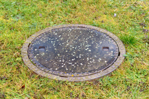 Manhole cover on a rural septic tank or sewage outlet set into a grassy field or lawn in a close up view