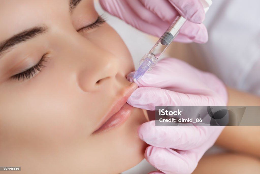 The doctor cosmetologist makes Lip augmentation procedure of a beautiful woman in a beauty salon The doctor cosmetologist makes Lip augmentation procedure of a beautiful woman in a beauty salon.Cosmetology skin care. Human Lips Stock Photo